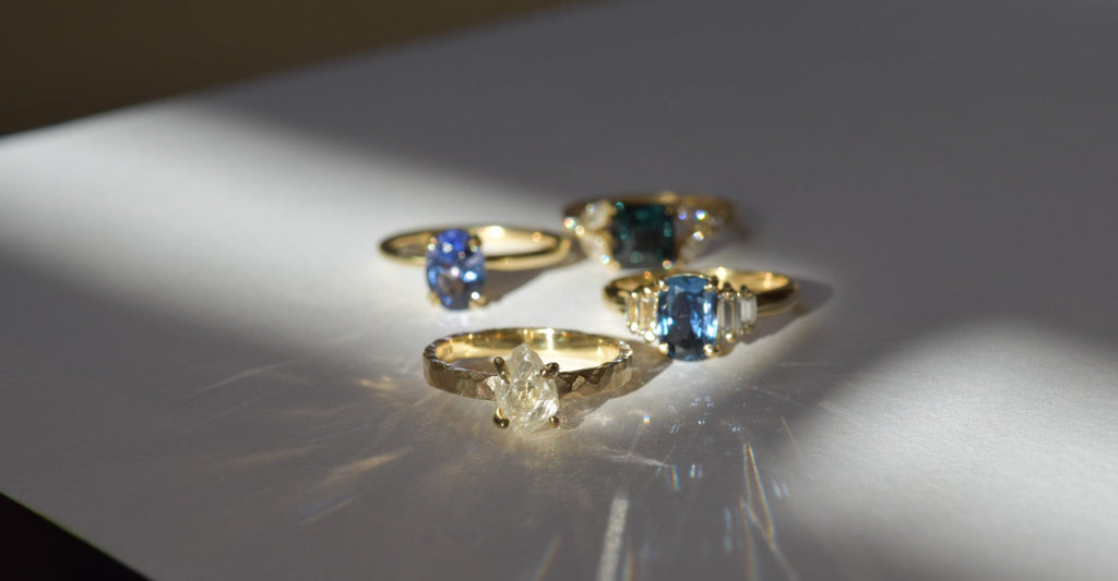 Four unique raw diamond rings in yellow gold, displayed on a white surface with light reflections highlighting their custom designs.