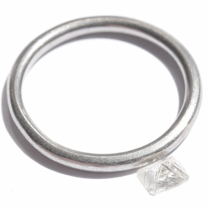 0.24 carat half octahedron white raw diamond next to platinum wedding band