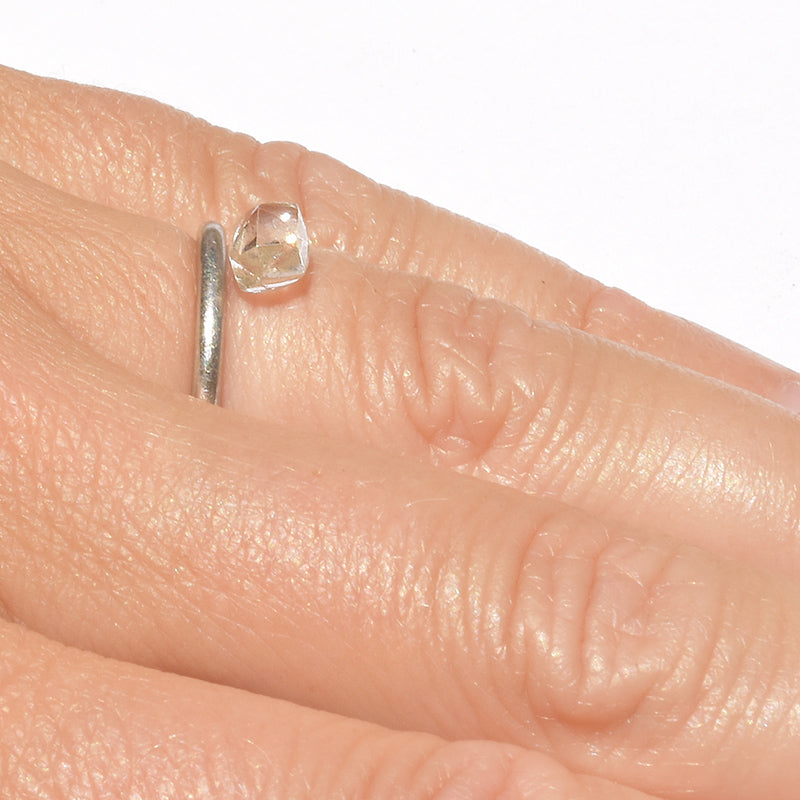 raw diamond in a dodecahedral shape on a hand next to a platinum ring