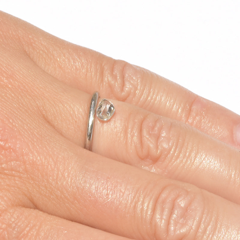 rough diamond in a rhombododecahedral shape on a hand next to a platinum wedding band